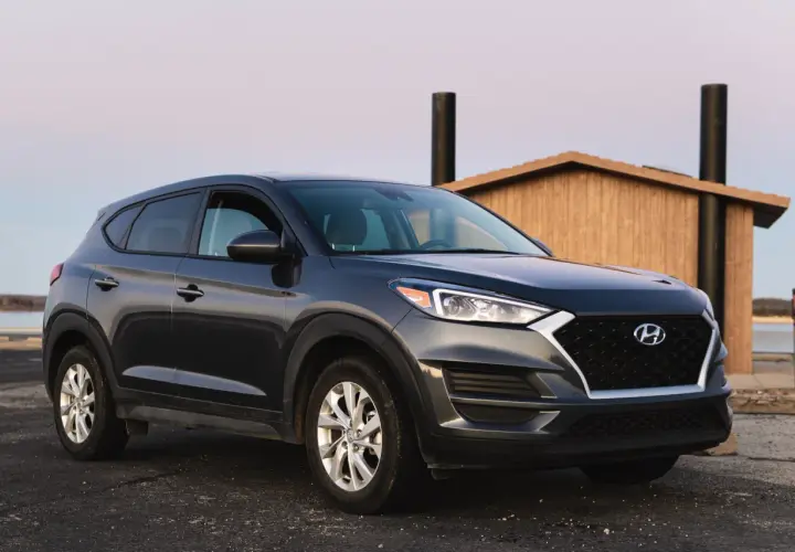 Ciemnoszary Hyundai Tucson zaparkowany przy drewnianej budowli. Zastanawiasz się, ile pali ten model?