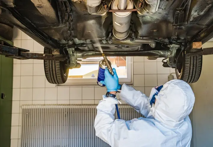 Mechanik w kombinezonie ochronnym zabezpiecza podwozie auta. Zastanawiasz się, ile kosztuje przegląd samochodu z gazem?