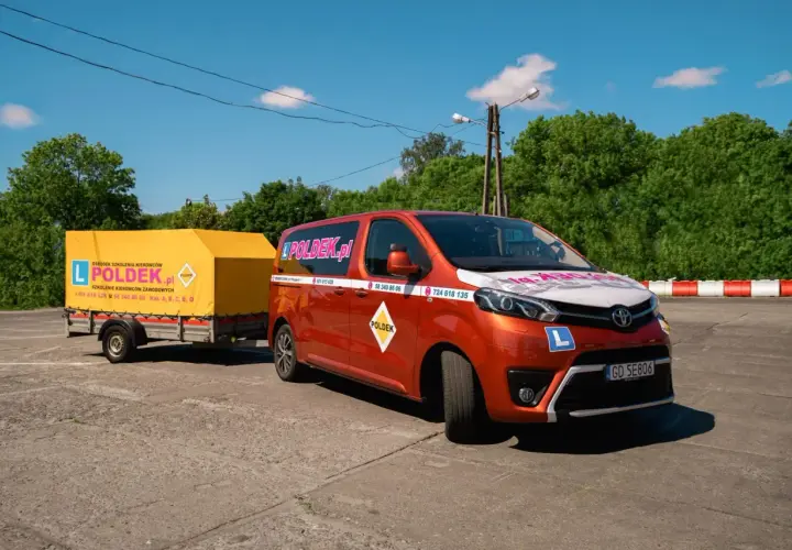 Pomarańczowy van z przyczepą szkoleniową "POLDEK.pl" na placu manewrowym.