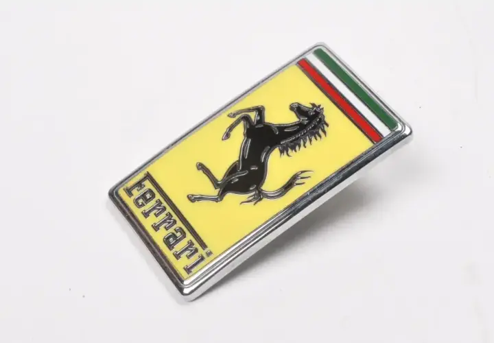 Oto jak wygląda znaczek Ferrari: czarny koń na żółtym tle, z napisem "ferrari" i włoską flagą.