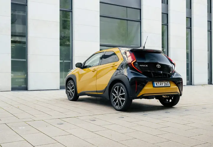 Żółto-czarny crossover Toyota Aygo X stoi na placu przed nowoczesnym budynkiem.
