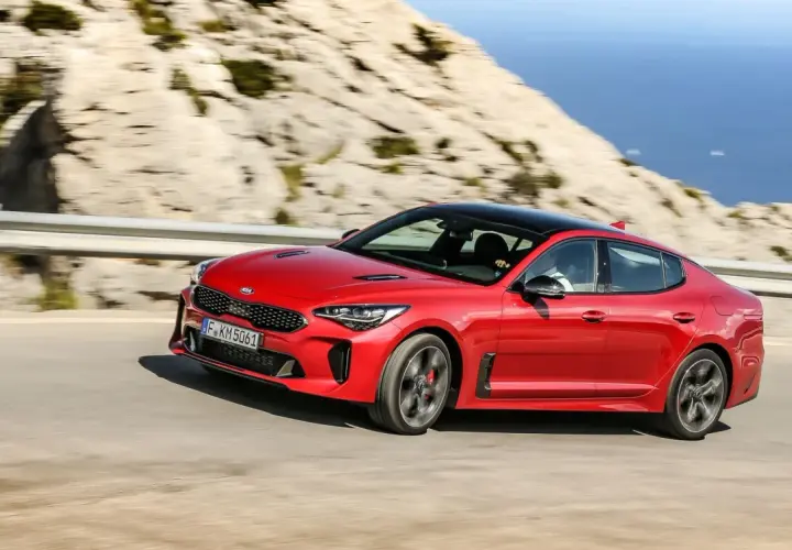 Czerwony Kia Stinger GT pędzi po krętej drodze z widokiem na morze.