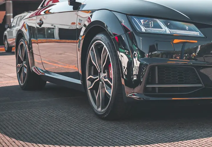 Zbliżenie na czarne, sportowe auto z widoczną felgą i oponą.