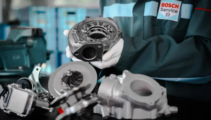 Mechanik w fartuchu Bosch Service prezentuje części turbosprężarki, pokazując jak sprawdzić turbinę.