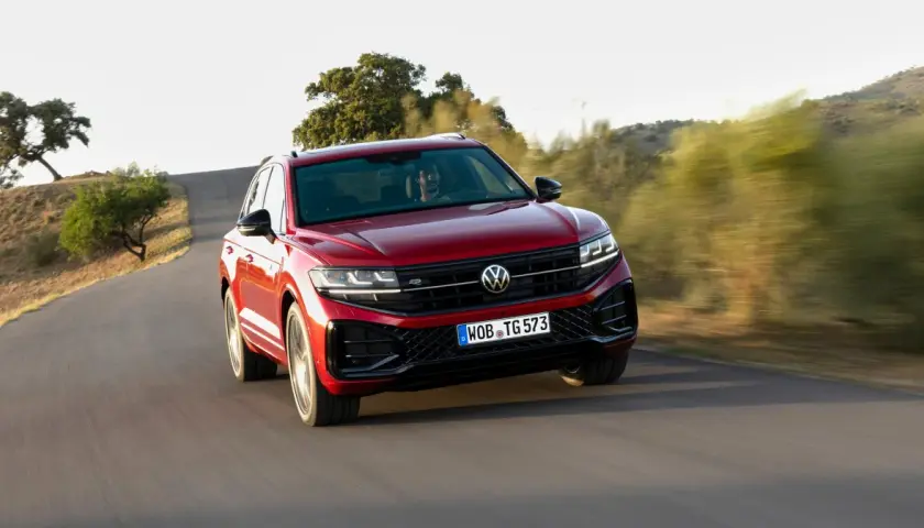 Czerwony Volkswagen Touareg 2024 pędzi po krętej drodze wśród wzgórz.