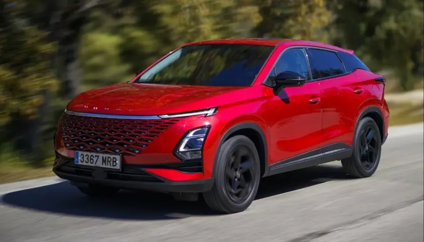 Czerwony, nowoczesny SUV, jeden z chińskich samochodów elektrycznych, jedzie po drodze wśród drzew.