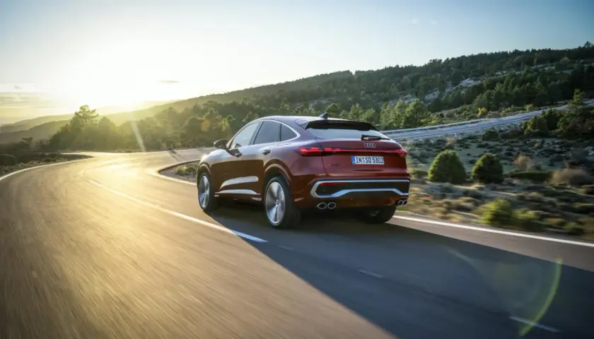 Czerwony samochód Audi coupe na krętej drodze w górach o zachodzie słońca.