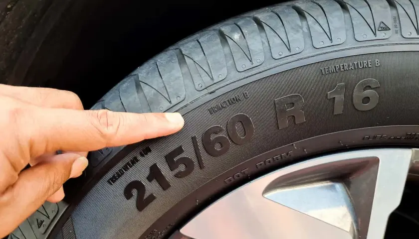 Palec wskazuje na oznaczenie opon 215/60 R16, informujące o rozmiarze i typie.