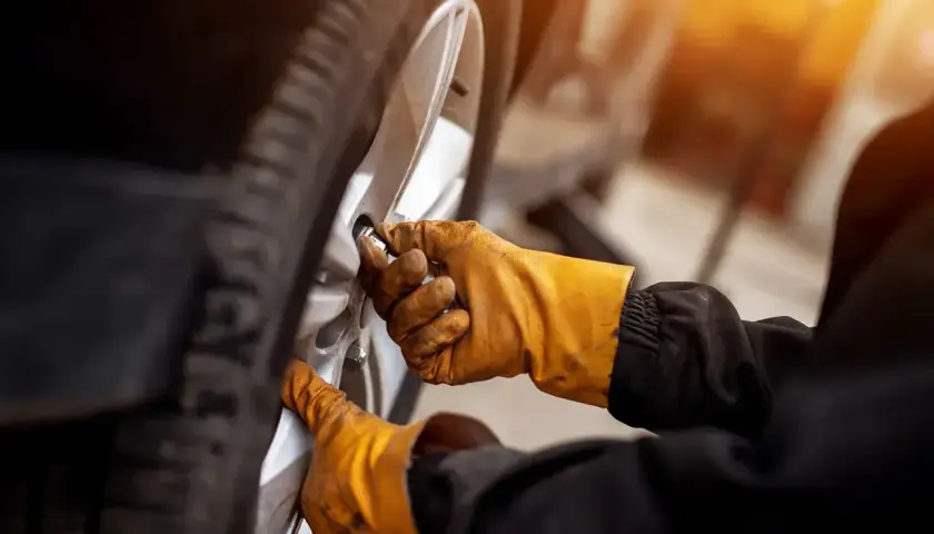 Ręce w żółtych rękawicach odkręcają śruby koła, przygotowując się do wymiany, jak wyjąć koło zapasowe Citroen Berlingo.
