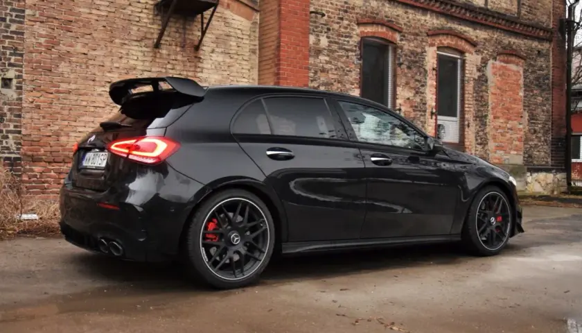 Czarny Mercedes-AMG A45s z dużym spojlerem i czerwonymi zaciskami hamulcowymi stoi przed starą ceglaną kamienicą.