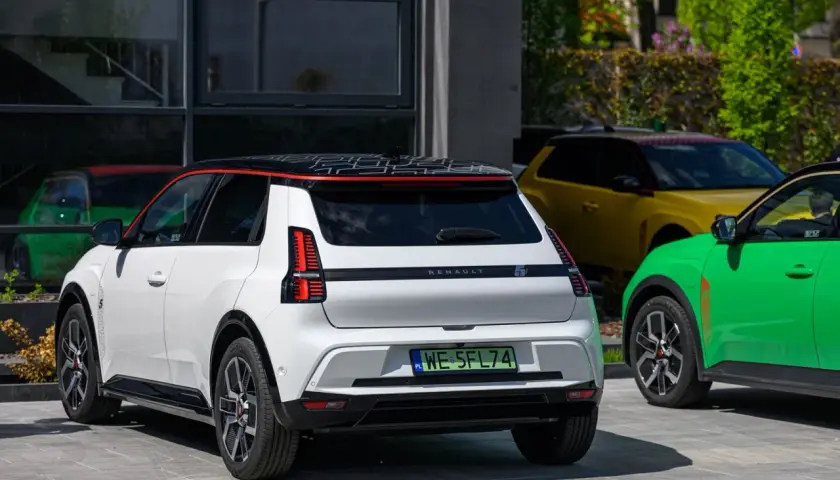 Biały Renault 5 E-Tech elektryczny z czarnym dachem i czerwonymi akcentami, obok zielonego i żółtego samochodu.