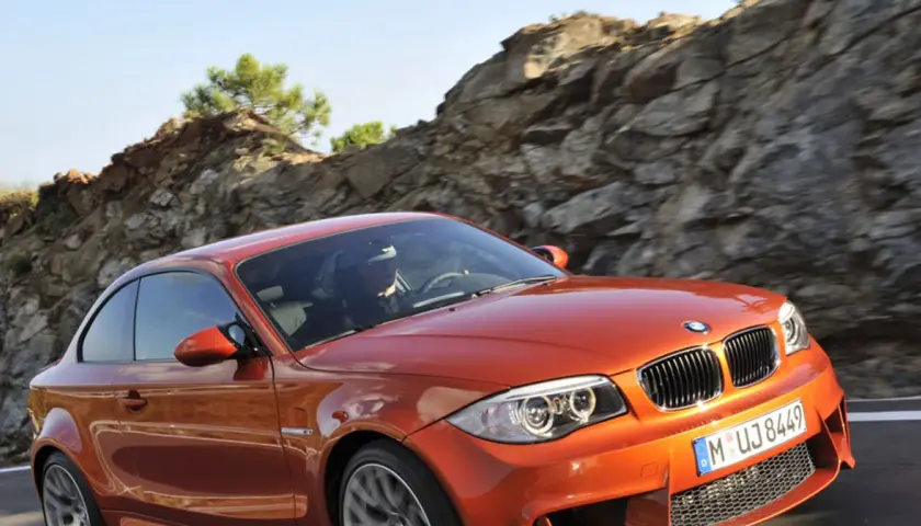 Pomarańczowy bmw1 z kierowcą za kierownicą pędzi po górskiej drodze.