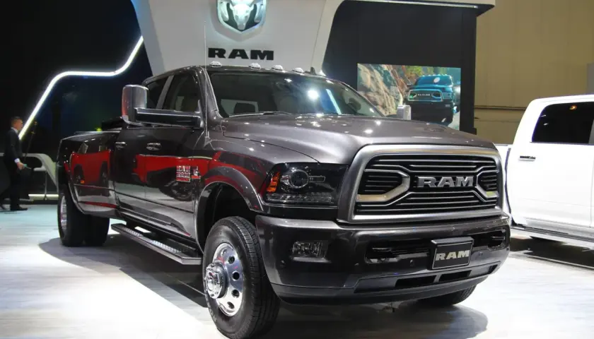 Ciemnoszary Dodge Ram 3500 z podwójnymi tylnymi kołami prezentuje się na wystawie, obok białego pickupa.