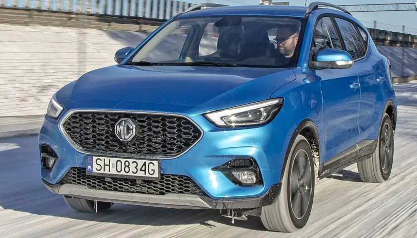 Niebieski MG ZS Classic jedzie po zaśnieżonej drodze. Kierowca w okularach prowadzi auto.