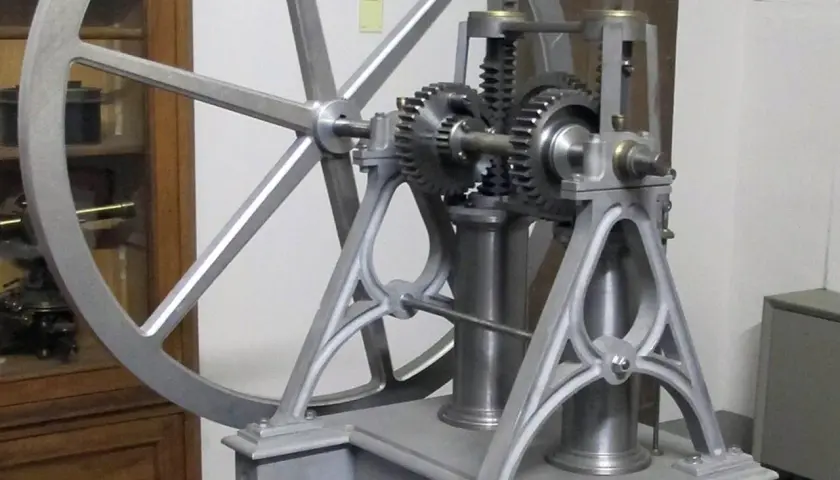 Mechanizm z kołem zamachowym i zębatkami, przypominający wczesne próby stworzenia silnika spalinowego.