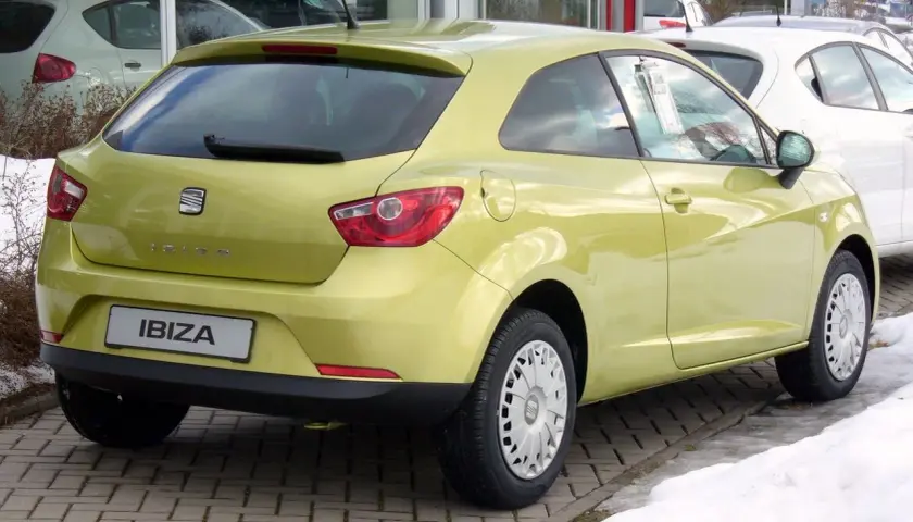 Jasnożółty Seat Ibiza 1.4 benzyna z tyłu, zaparkowany na kostce brukowej, obok śniegu.