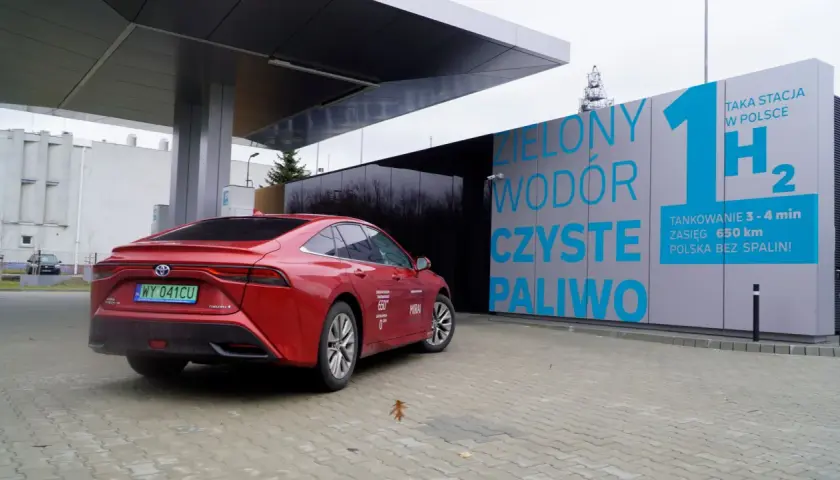 Czerwona Toyota Mirai na stacji tankowania wodoru. "Zielony wodór, czyste paliwo" - hasła na budynku stacji.