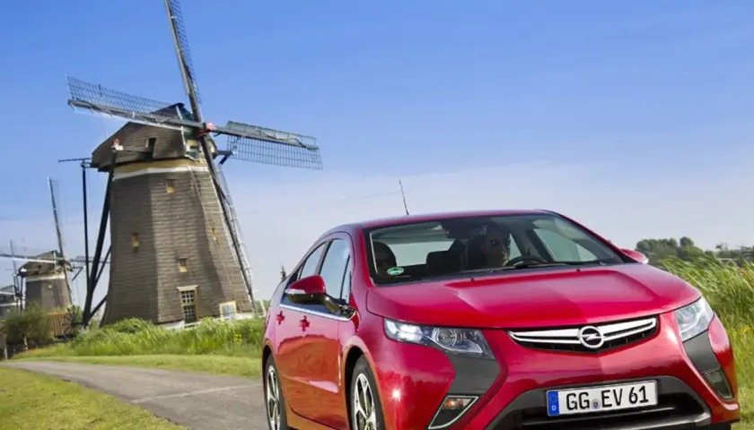 Czerwony Opel Ampera na tle wiatraków w Holandii.