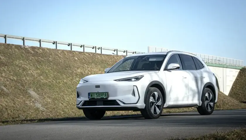 Biały Geely EX5 na tle słonecznego nieba i zielonych wzgórz. Elegancki SUV gotowy na podróż.