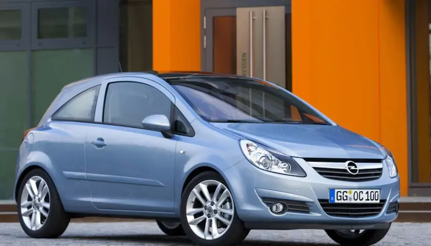 Niebieski Opel Corsa D 1.2 benzyna stoi przed pomarańczowym budynkiem.
