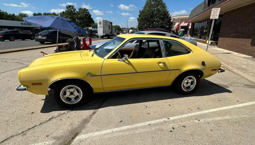 Żółty Ford Pinto z lat 70. stoi zaparkowany przy ulicy, obok sklepu.