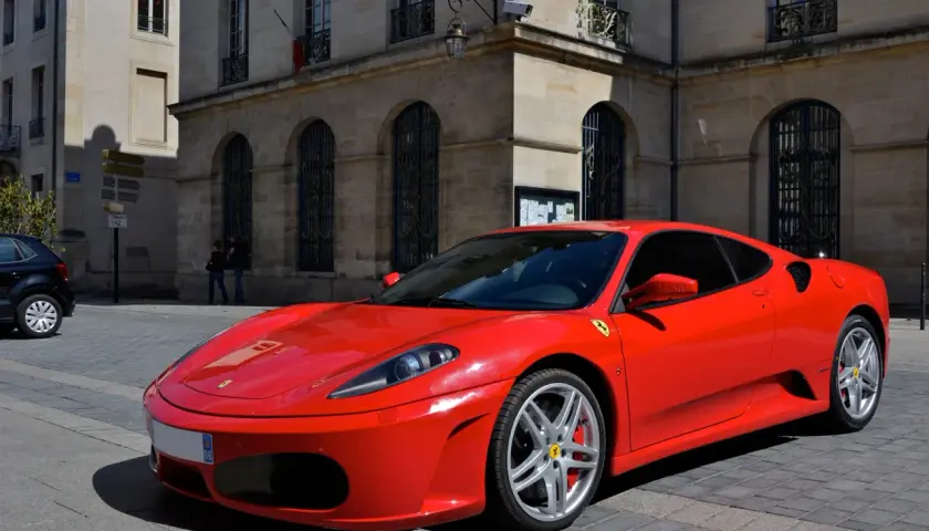 Czerwone Ferrari F430 zaparkowane na brukowanej ulicy przed kamienną kamienicą.