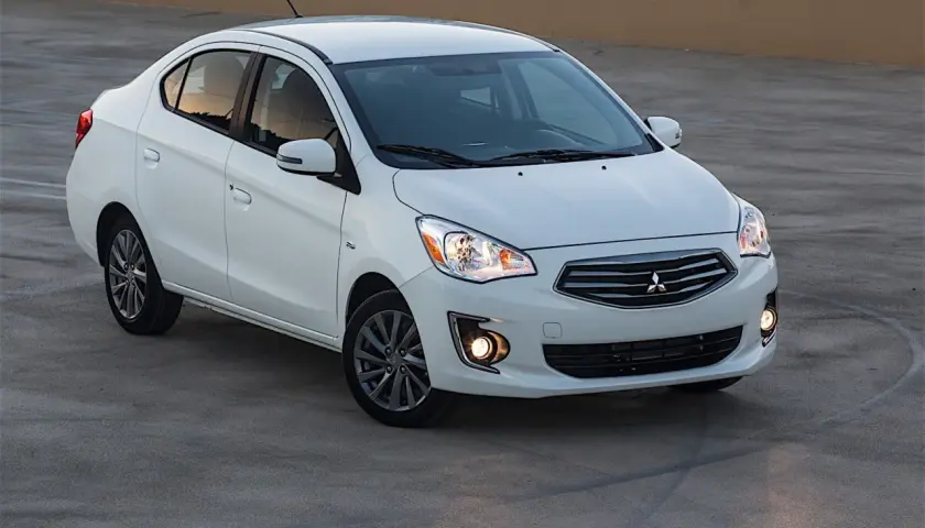 Biały sedan Mitsubishi Mirage zaparkowany na betonowej nawierzchni.