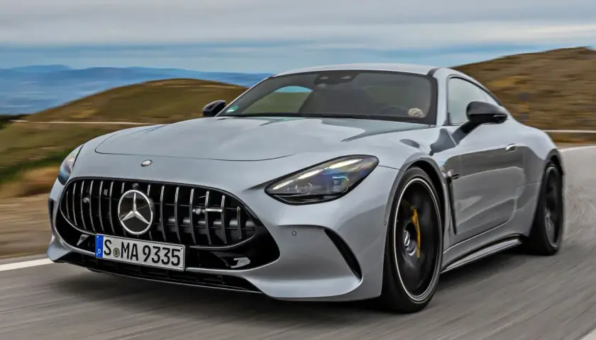 Srebrny Mercedes-AMG GT sunie po krętej drodze, ukazując swoją sportową sylwetkę i potężny grill.