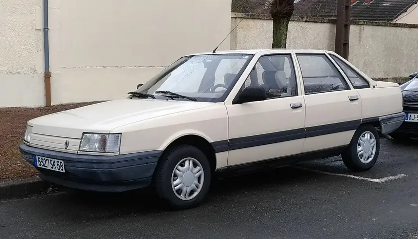 Jasny beżowy sedan Renault 21 z lat 80. stoi na mokrej drodze.