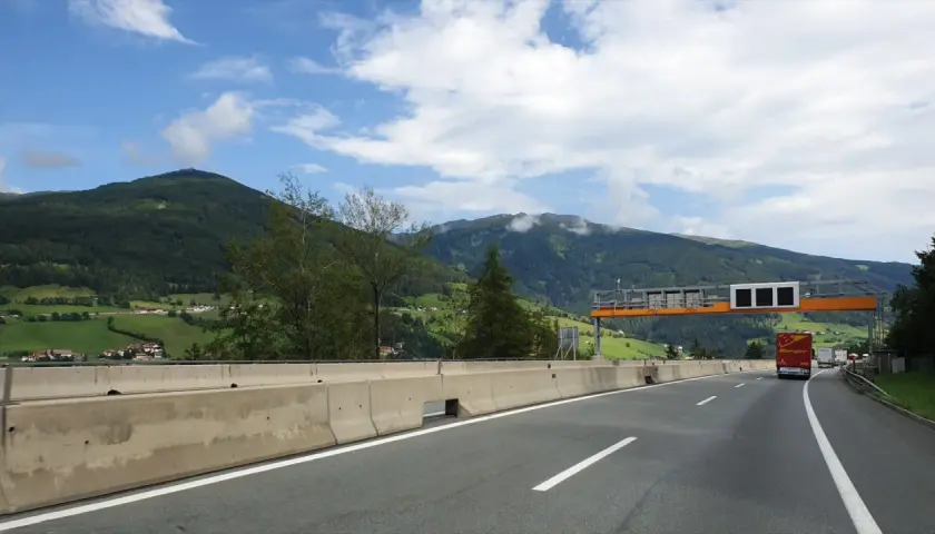 Autostrada w Austrii z widokiem na góry, znaki drogowe i ciężarówka.