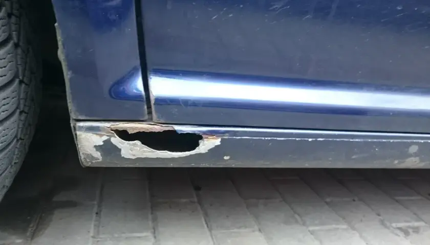 Widoczne są poważne dziury w progach niebieskiego samochodu, co pokazuje, jak załatać dziury w samochodzie.