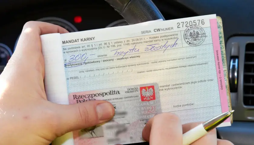 Mandat karny na 300 zł za wykroczenie. W tle widać fragment deski rozdzielczej samochodu, sugerujący, że zdarzenie miało miejsce na skrzyżowaniu.