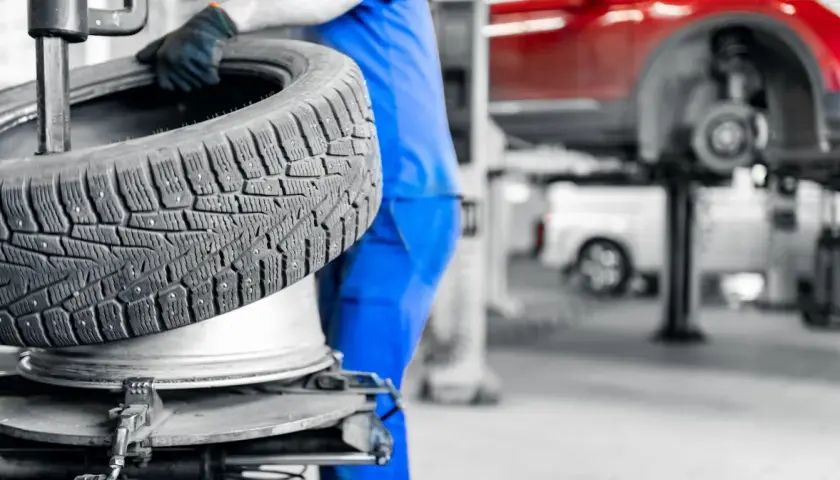 Mechanik w niebieskim kombinezonie wymienia oponę. Dowiedz się, ile kosztuje wymiana opon w Twojej okolicy.