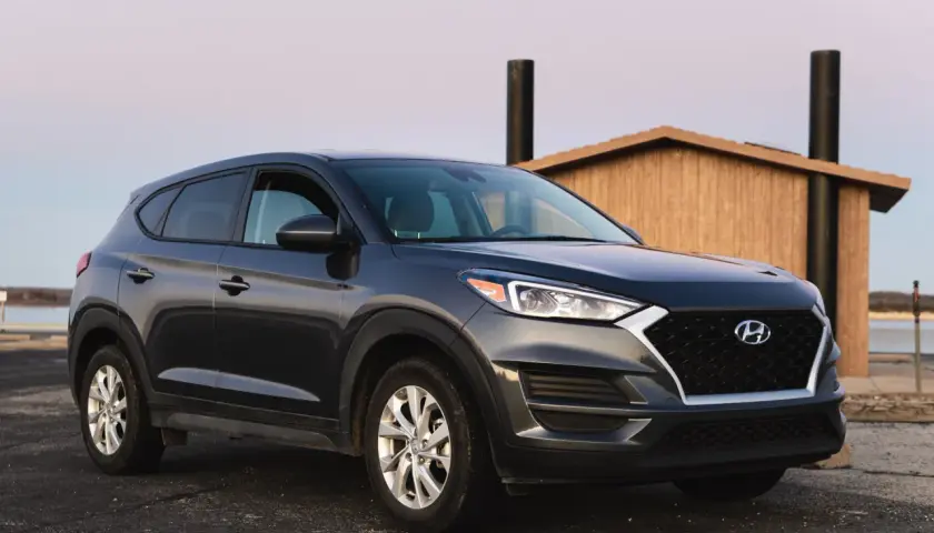 Ciemnoszary Hyundai Tucson zaparkowany przy drewnianej budowli. Zastanawiasz się, ile pali ten model?