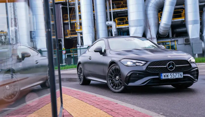 Ciemnoszary Mercedes-Benz CLE Coupé na tle przemysłowych rur i budynków.