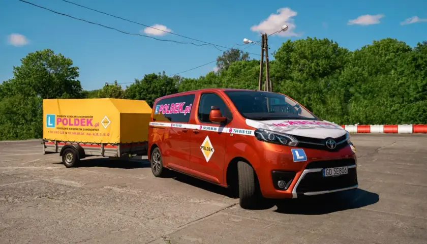 Pomarańczowy van z przyczepą szkoleniową "POLDEK.pl" na placu manewrowym.