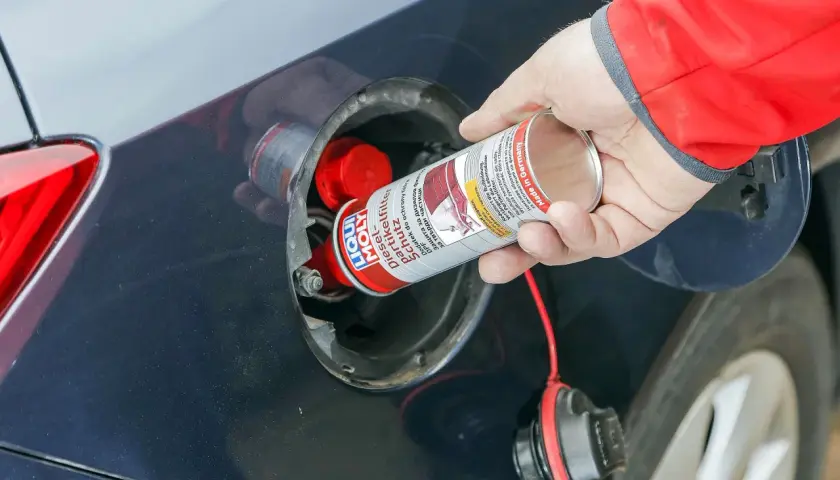 Ręka wlewa dodatek do diesla DPF do baku samochodu. Preparat chroni filtr cząstek stałych.