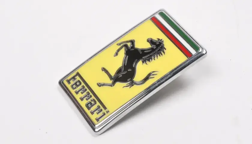 Oto jak wygląda znaczek Ferrari: czarny koń na żółtym tle, z napisem "ferrari" i włoską flagą.