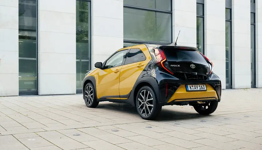 Żółto-czarny crossover Toyota Aygo X stoi na placu przed nowoczesnym budynkiem.