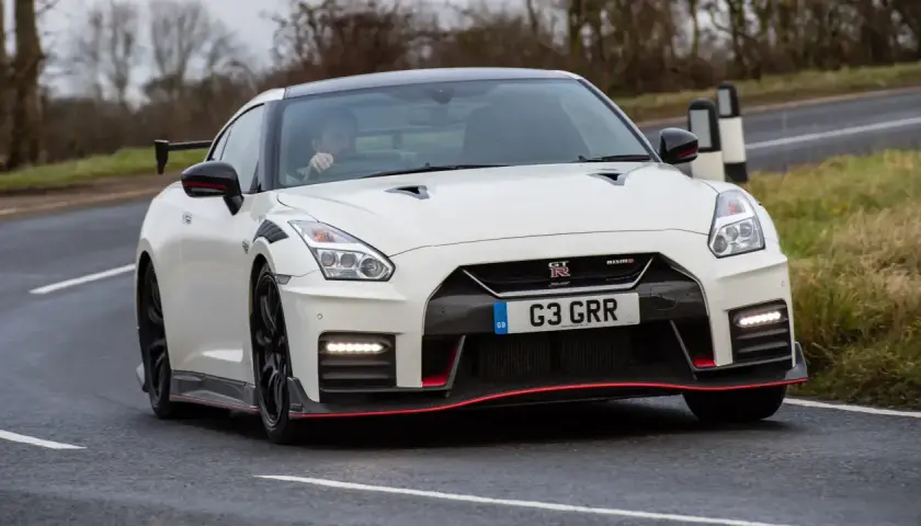 Biały Nissan GT-R Nismo z czerwonymi akcentami pędzi po drodze.