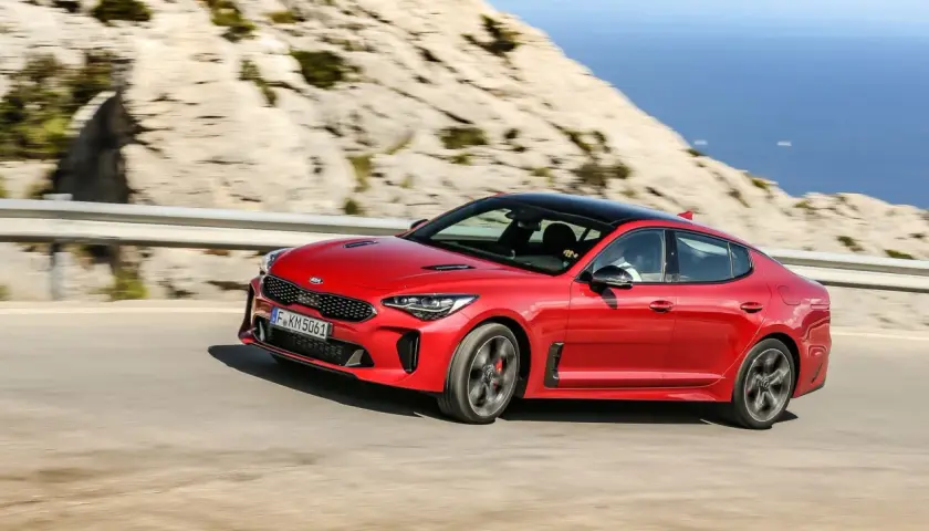 Czerwony Kia Stinger GT pędzi po krętej drodze z widokiem na morze.