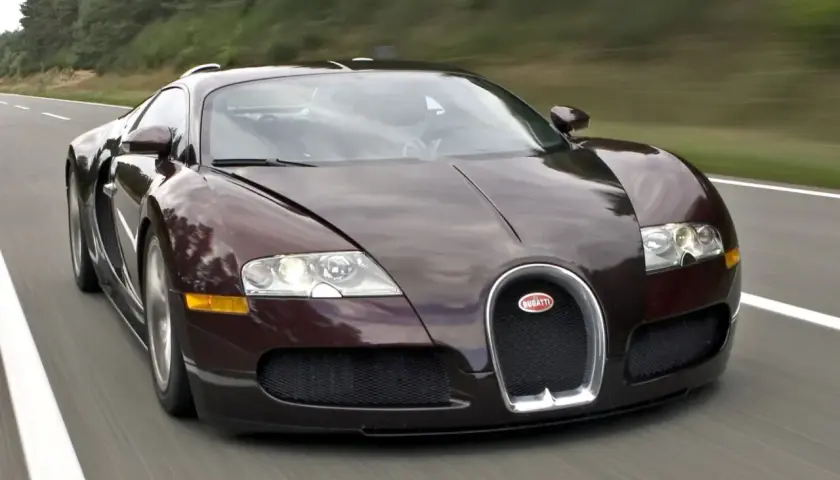 Ciemnobrązowy Bugatti Veyron pędzi po drodze. Ten hipersamochód ma 16 cylindrów, co przekłada się na jego niesamowitą moc.