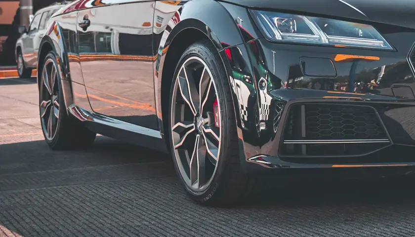 Zbliżenie na czarne, sportowe auto z widoczną felgą i oponą.