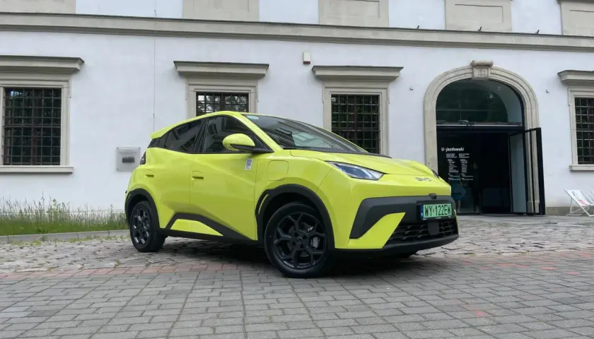 Jaskrawożółty BYD Seagull zaparkowany na bruku przed budynkiem z łukowym wejściem.