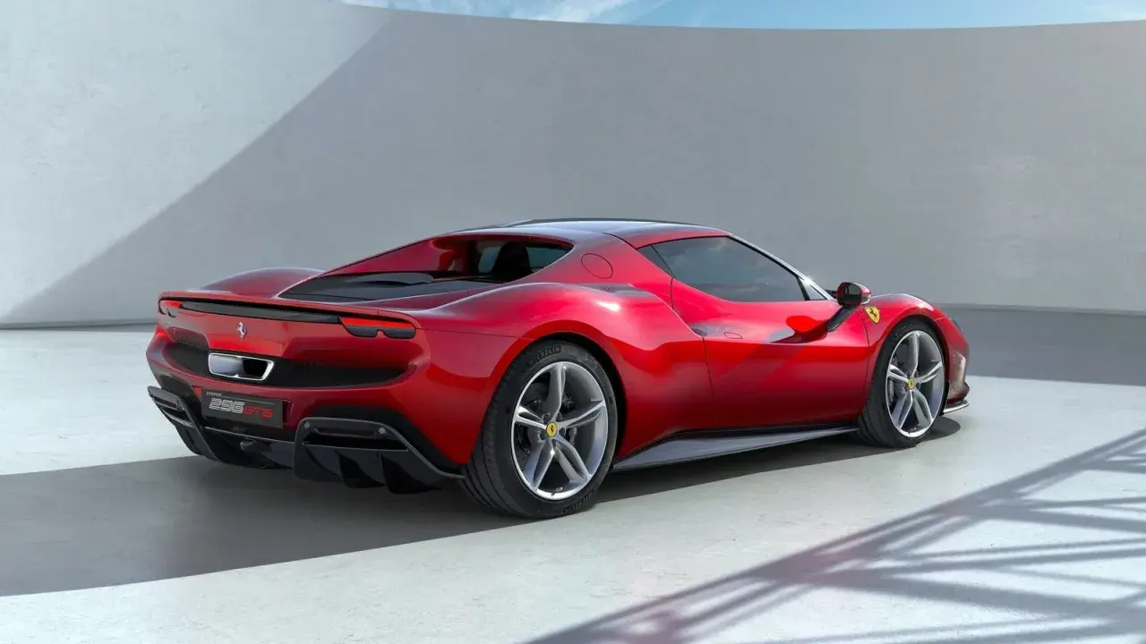 Czerwone Ferrari 296 GTB widziane z tyłu, na tle białej ściany i nieba.