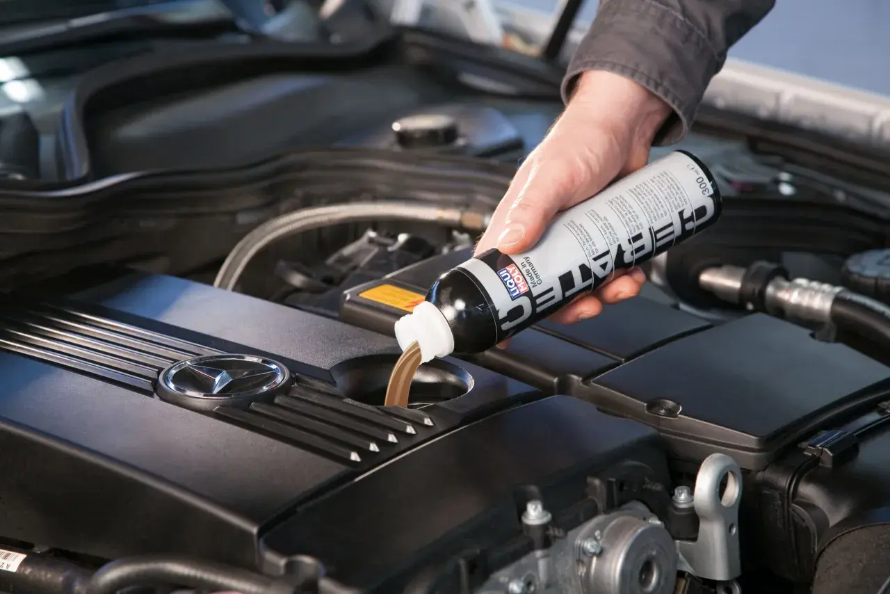 Dłoń wlewa płyn spulung liqui moly do silnika samochodu.