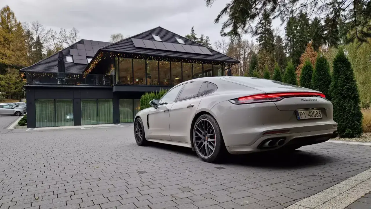 Białe Porsche Panamera GTS przed nowoczesnym budynkiem z panelami słonecznymi. Idealny wybór dla firm ceniących leasing operacyjny.
