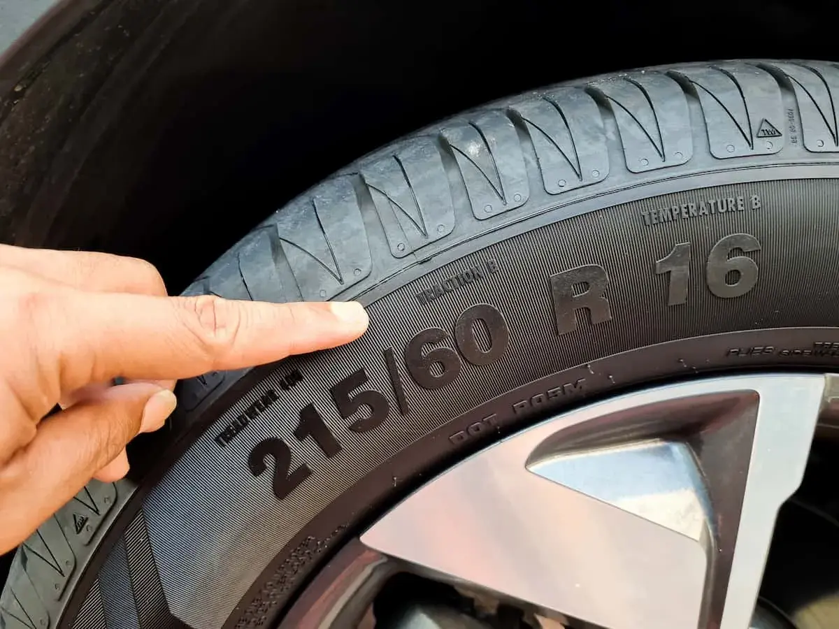 Palec wskazuje na oznaczenie opon 215/60 R16, informujące o rozmiarze i typie.