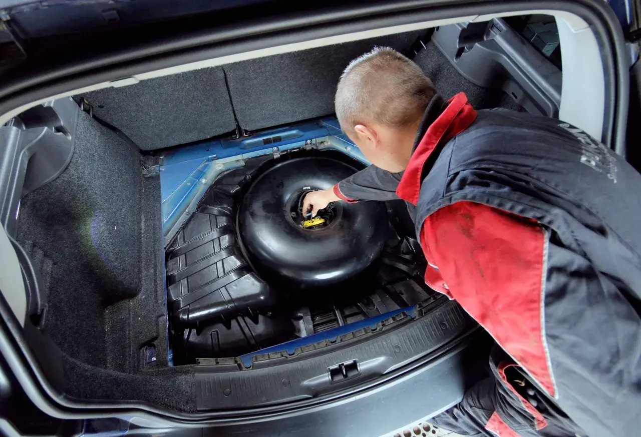Mechanik sprawdza butlę LPG w bagażniku. Dowiedz się, ile kosztuje legalizacja butli LPG i jakie są wymagania.