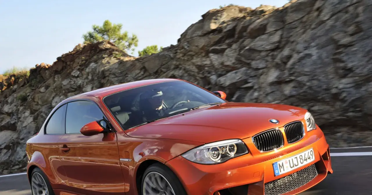 Pomarańczowy bmw1 z kierowcą za kierownicą pędzi po górskiej drodze.